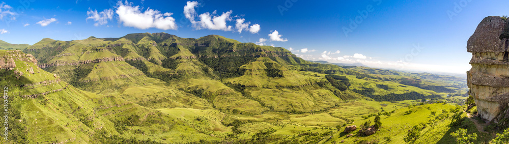 Naklejka premium Panorama over soft green mountains, on a sunny day, on the right hand is a rock formation called Sphinx, Drakensberg, Giants Castle Game Reserve, South Africa