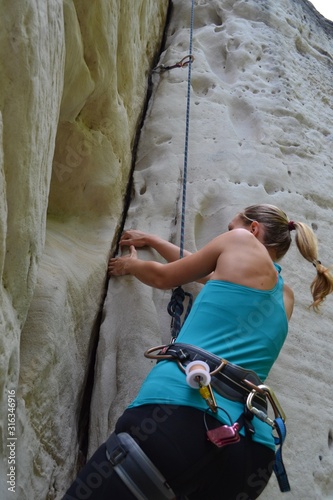 Young girl in blue top and blond ponytail climbs crack on the sandstone rock. Bohemian Paradise, Czech Republic.