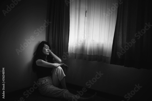 depress woman sitting on floor in room near window in white tone, sadness and depress concept