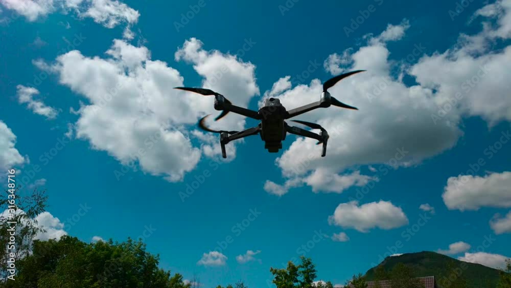 A drone floating in the air with propellers against a background of white clouds and a blue sky. A drone floating in the air with propellers against a background of white clouds and a blue sky.
