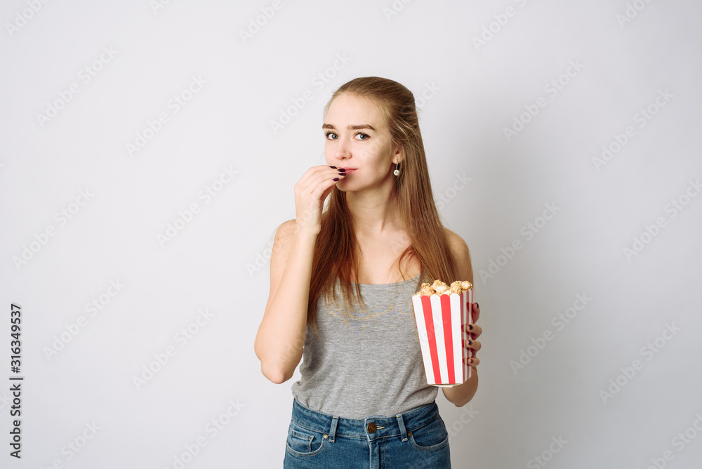 Cute girl holding popcorn and looking at camera isolated on white studio. Excited woman having popcorn while watching movie on white background Cute girl holding popcorn and looking at camera isolated on white studio. Excited woman having popcorn while watching movie on white background