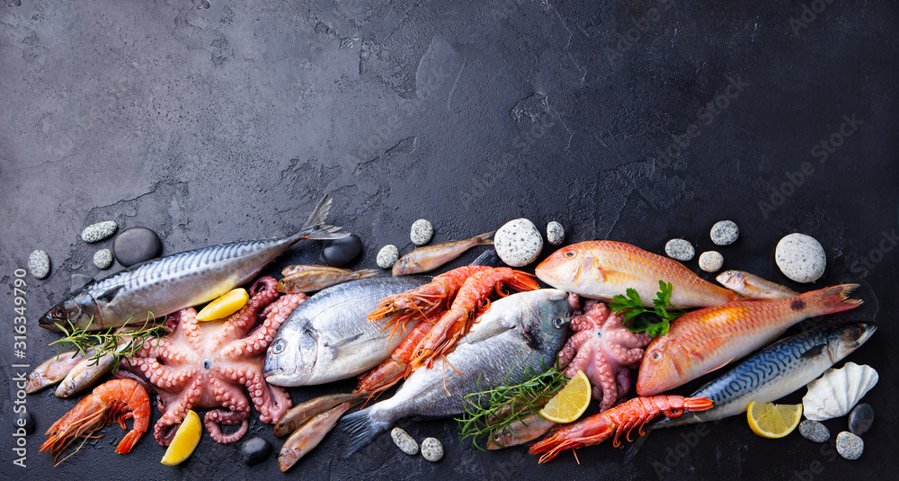 Fresh fish and seafood assortment on black slate background. Copy space. Top view.