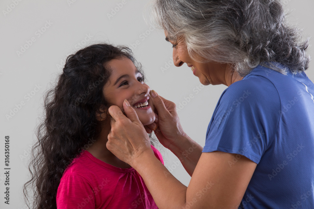 Portrait of a happy grandmother pulling her grand-daughter’s cheeks. Portrait of a happy grandmother pulling her grand-daughter’s cheeks.