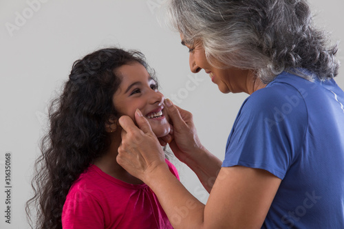 Portrait of a happy grandmother pulling her grand-daughter’s cheeks. 