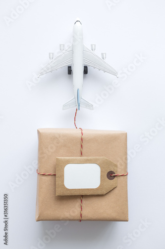 Cardboard delivery box with copy space label and small airplane abstract on white.