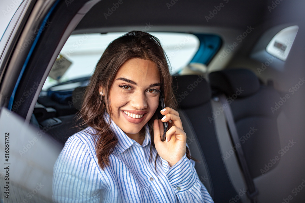 Young businesswoman talking on the phone in the back seat of the car. Close up portrait of young business woman sitting on back seat of the car and laughing while talking on mobile phone Young businesswoman talking on the phone in the back seat of the car. Close up portrait of young business woman sitting on back seat of the car and laughing while talking on mobile phone