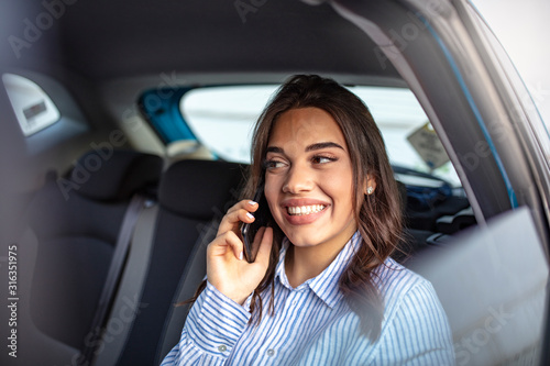 Cute young woman traveling. Attractive business woman in car. Talking on her mobile phone. Happy business woman talking on phone. Cheerful pretty young woman talking on phone and look straight ahead. © Dragana Gordic