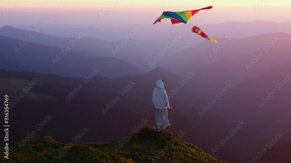 Young girl with kite standing on top of mountain amazing view outdoor woman happiness happy landscape hiking sky meadow grass sunlight free travel relax active wind slow motion