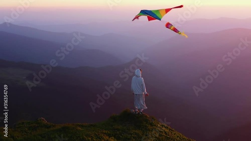 Young girl with kite standing on top of mountain amazing view outdoor woman happiness happy landscape hiking sky meadow grass sunlight free travel relax active wind slow motion