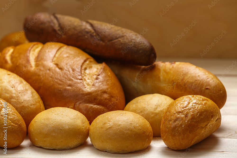 Loaf of bread, baguette and buns on a wooden background