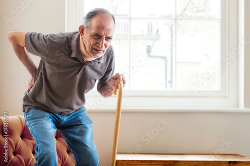 Фотография Senior man having a knee pain trying to stand up at home