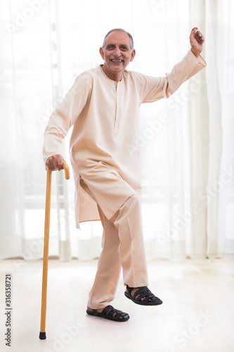 Happy senior man dancing with the walking stick at home. (Health and fitness) 