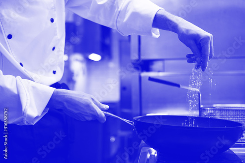 Unrecognizable cook salt food in frying pan in kitchen, phantom blue