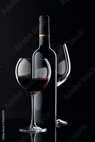 Bottle and glasses of red wine on a black background.