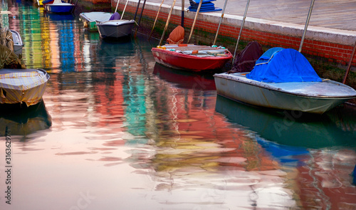 Colorful reflection in canal water of anchored motor boats and painted in vibrant colors houses' facades in Burano, Italy. © trialartinf