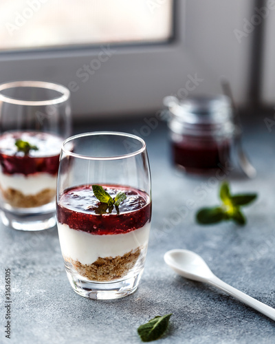 Two layered dessrts in glasses with granola, yogurt and berry jam