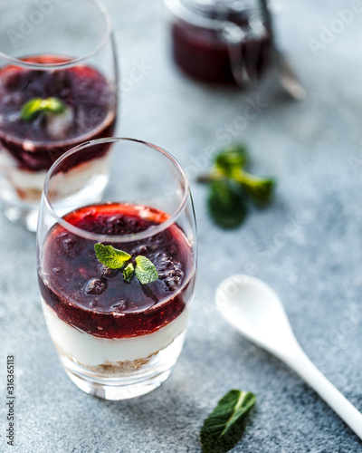 Two layered dessrts in glasses with granola, yogurt and berry jam