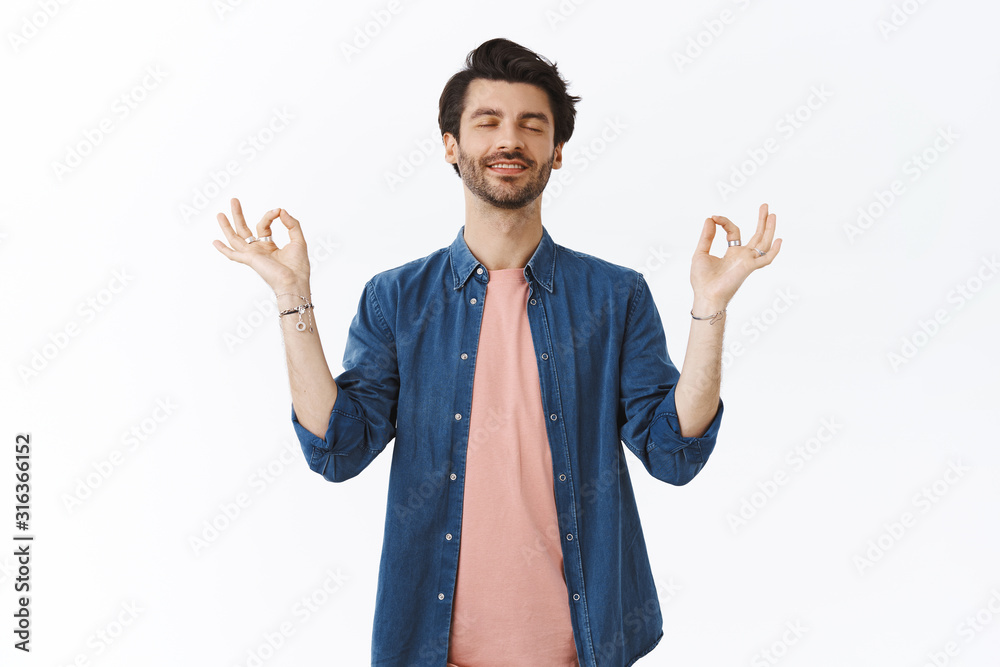 Happy relieved bearded guy reaching nirvana, calm down as meditating. Man with closed eyes in lotus pose with zen signs, smiling as practice yoga, breathe relaxed, soothing stress, white background