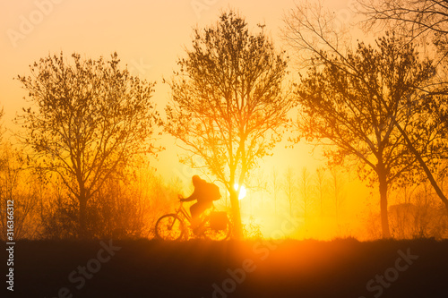 Fietser langs de Schelde tijdens een heerlijke zonsopkomst met een laagje mist in de Zevergemse Scheldemeersen.