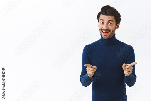 Stylish good-looking bearded man in blue high neck sweater, pointing at camera and smiling delighted, encourage employers during meeting, businessman explain chart and main concept