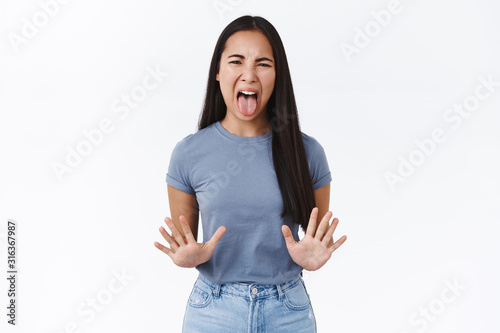 Disgusted asian girl refusing something awful, express aversion, squinting, cringe from reek, smell something bad, shaking hands in no, rejection, wrinkle nose, want puke, white background photo