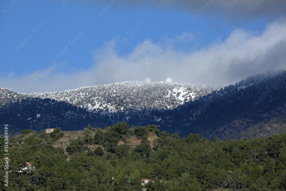 Trodos mountains under snow seen from valley, blue sky with heavy gray clouds, Cyprus