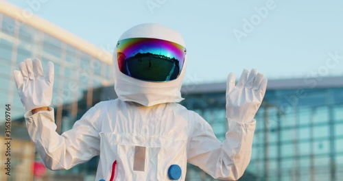 Portrait of the man or a woman in the full costume of astronaut with head armor waving with hands to the camera before going to the outer space in a rocket. Outdoors. photo