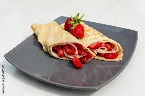 Rolled crepes or balkan pancakes stuffed fresh chopped strawberries. Gourmet sweet dish