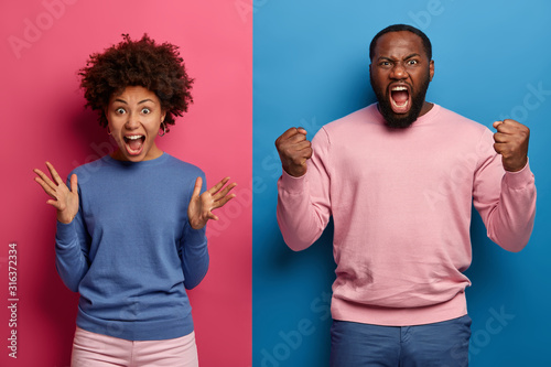 Photo of annoyed rude woman and man scream with agression, grimace and gesture angrily, dont agree with not fair situation, roar loudly I will kiss you, stand against two color studio background photo