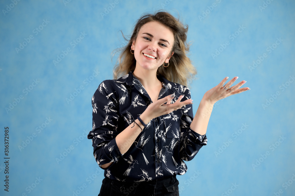 Concept woman in a dark blouse smiling talking. Portrait of a model girl with excellent makeup with curly hair and good teeth in the studio on a blue background. Concept woman in a dark blouse smiling talking. Portrait of a model girl with excellent makeup with curly hair and good teeth in the studio on a blue background.