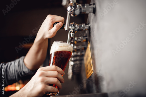 Bartender pours beer from tap into glass  dark background. Alcohol craft drink concept