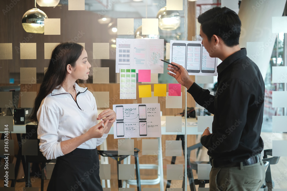 Obraz premium Two Asian application designers work together to brainstorm, outline, and develop mobile applications.