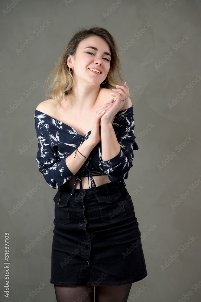 Fototapeta premium Concept woman in a dark suit smiles and talks. Vertical portrait of a girl model with excellent makeup with good teeth in the studio on a gray background.
