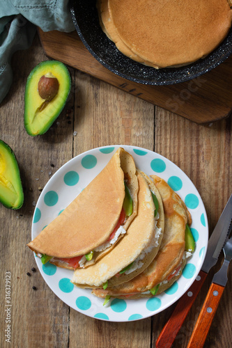 The concept of a healthy breakfast or snack. Oat pancakes stuffed with cottage cheese, salmon and avocado in a plate on rustic wooden table. Top view flat lay background.