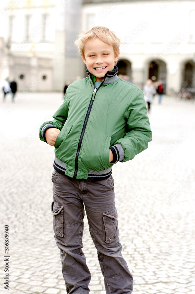 A boy smiles into the camera in a cityscape which is only hinted at by over-exposure