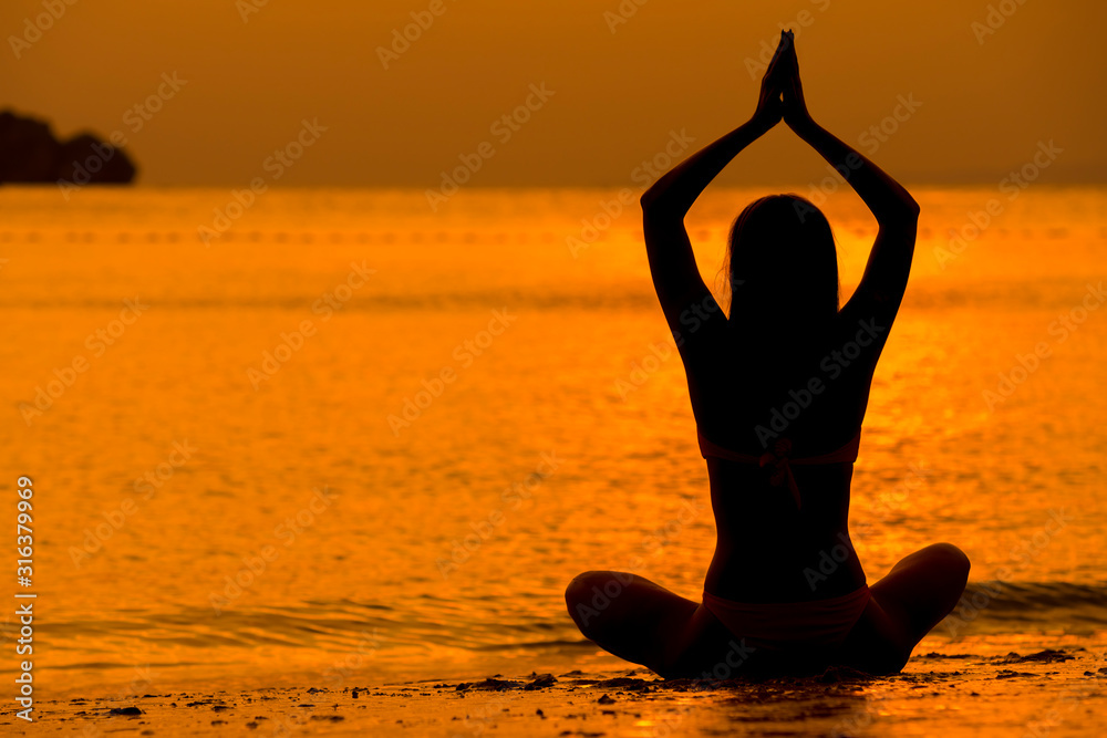 Young women meditate while doing yoga meditation, spiritual mental health practice with silhouette of lotus pose having peaceful mind relaxation on sea outdoor with sunset golden heavenly.