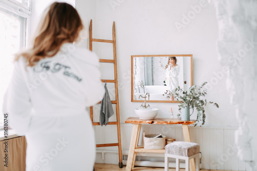 Morning of the bride. Happy beautiful with a snow-white smile and red lips girl in a white robe and with a towel on her head sitting laughing and having fun in the bath on a white background, relax
