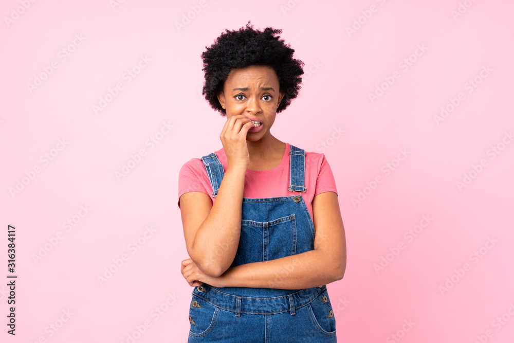 African american woman with overalls over isolated pink background nervous and scared
