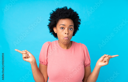 African american woman over isolated blue background pointing to the laterals having doubts