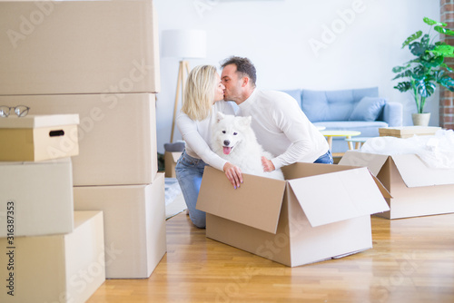 Young beautiful couple with dog kissing sitting on the floor at new home around cardboard boxes