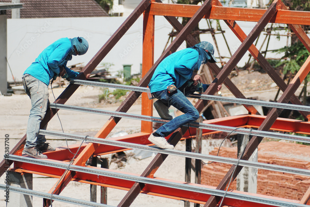 worker holding electric drill working and installing structure of Galvanized steel pipe, roof steel on roof structure on construction site
