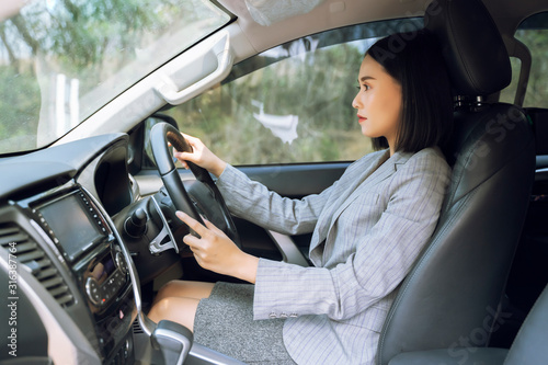 Safety driving concept, Smiling happy young  Chinese Thai Asian businesswoman driving a car in town, Confident and beautiful girl. Rear view  woman in business suit wear looking over her shoulder