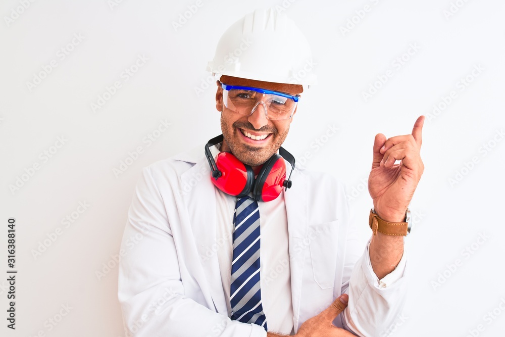 Young chemist man wearing security helmet and headphones over isolated background with a big smile on face, pointing with hand and finger to the side looking at the camera. Young chemist man wearing security helmet and headphones over isolated background with a big smile on face, pointing with hand and finger to the side looking at the camera.