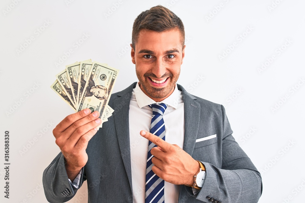 Young handsome business man holding bunch of dollars banknotes over isolated background very happy pointing with hand and finger Young handsome business man holding bunch of dollars banknotes over isolated background very happy pointing with hand and finger