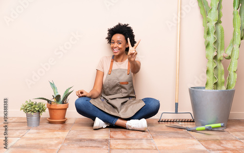 Gardener woman sitting on the floor smiling and showing victory sign