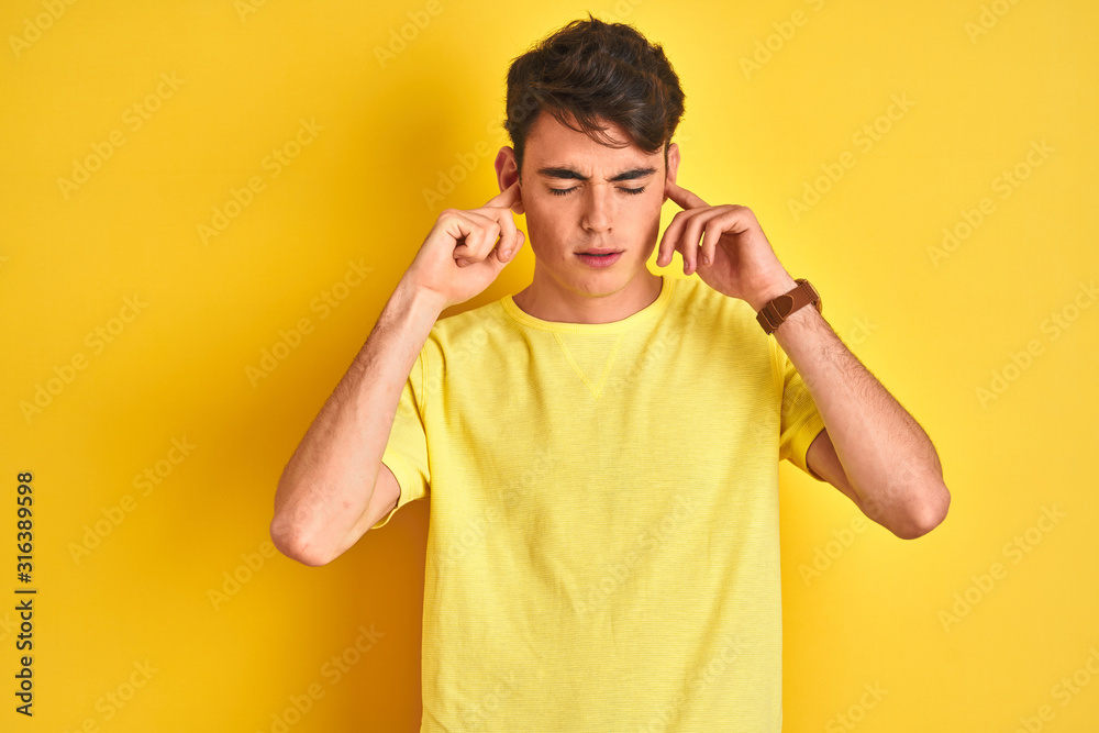 Teenager boy wearing yellow t-shirt over isolated background with hand on head for pain in head because stress. Suffering migraine. Teenager boy wearing yellow t-shirt over isolated background with hand on head for pain in head because stress. Suffering migraine.