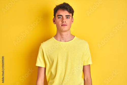 Teenager boy wearing yellow t-shirt over isolated background Relaxed with serious expression on face. Simple and natural looking at the camera.