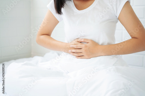 Asian woman unhappy lying on the bed looking sick, suffers from stomach ache in the bedroom, stomachache because of menstruation and eating spoiled food, Chronic gastritis. Abdomen bloating concept