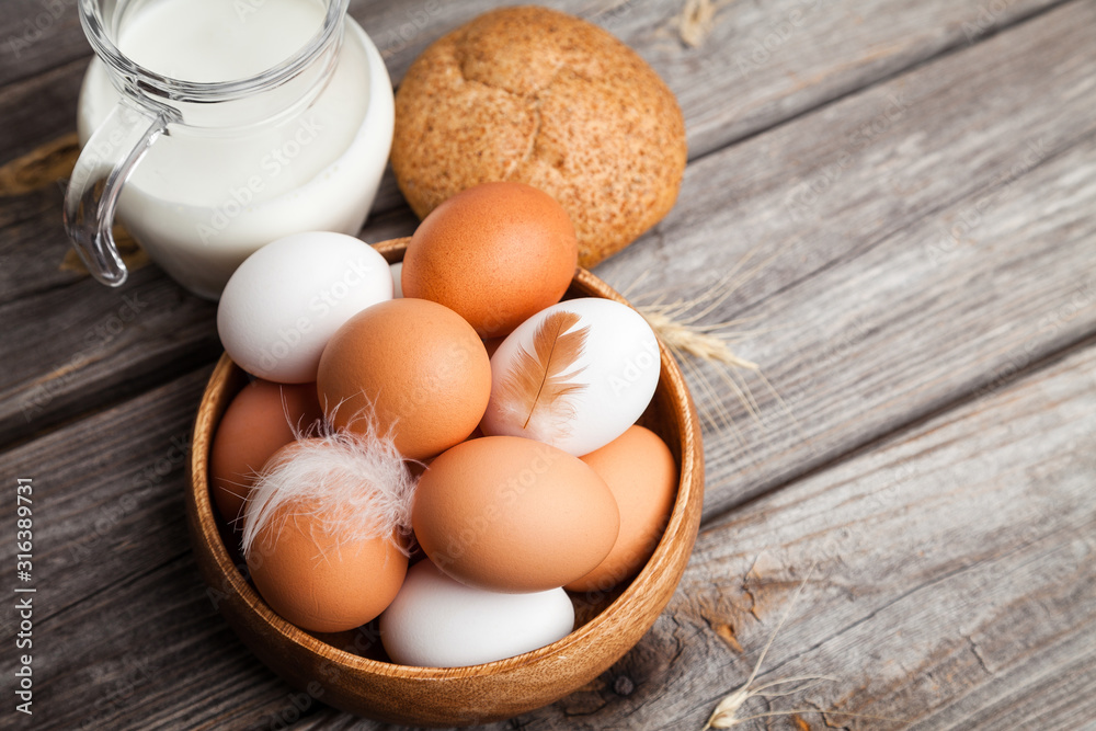 Fresh white and brown chicken eggs in a wooden bowl, milk, bread, and wheat ears. Raw eggs on wooden background Fresh white and brown chicken eggs in a wooden bowl, milk, bread, and wheat ears. Raw eggs on wooden background