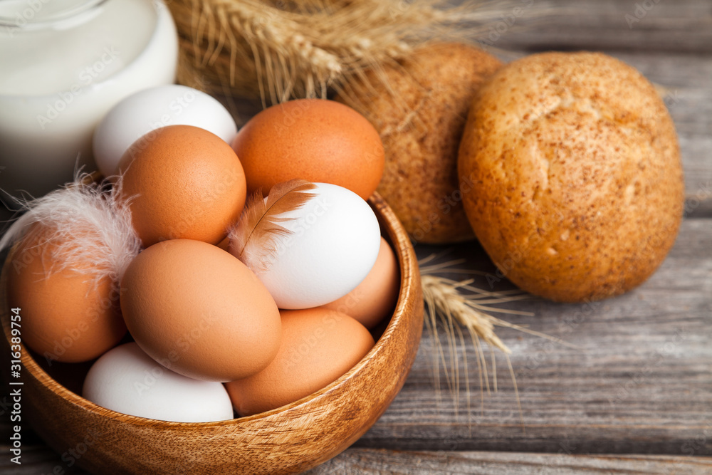 Fresh white and brown chicken eggs in a wooden bowl, milk, bread, and wheat ears. Raw eggs on wooden background Fresh white and brown chicken eggs in a wooden bowl, milk, bread, and wheat ears. Raw eggs on wooden background